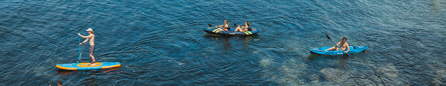 Trois images distinctes illustrent la diversité des planches de stand up paddle Wattsup. Dans la première image, la planche Wattsup Lined 10’2 est mise en avant, flottant gracieusement sur une eau bleu clair, avec en premier plan la pagaie incluse en accessoire. La deuxième image présente un ensemble de trois planches de SUP Wattsup naviguant sur une mer bleu foncé, la planche Wattsup Lined 10’2 étant positionnée à l'extrême gauche de la composition. Enfin, dans la dernière image, une jeune femme est vue portant sa planche de SUP grâce à la poignée de confort située au centre de la planche, avec le leash attaché à l'arrière, offrant une illustration vivante de l'utilisation pratique et polyvalente de ces équipements